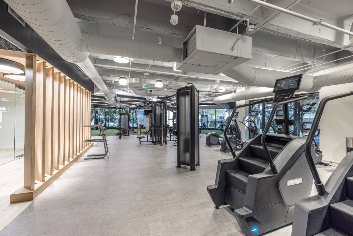 Finished fitness amenity build-out by i30 Builders: open training floor with cardio equipment, exposed structure, and a slatted timber screen.