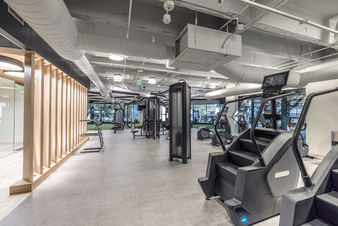 Completed fitness amenity build-out with cardio equipment, strength stations, and open-ceiling commercial finishes.