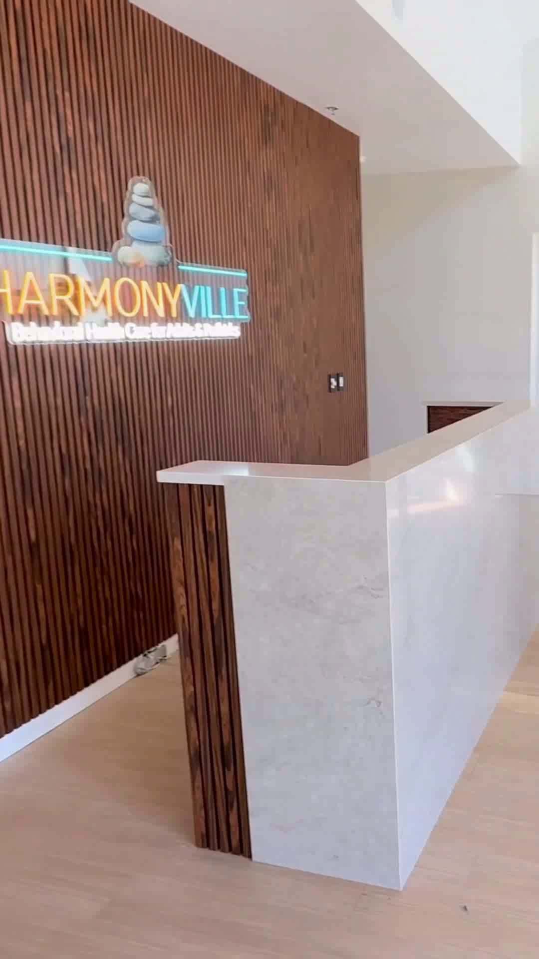 Finished tenant-improvement office reception by i30 Builders: a marble reception desk and walnut slat feature wall with illuminated brand signage.