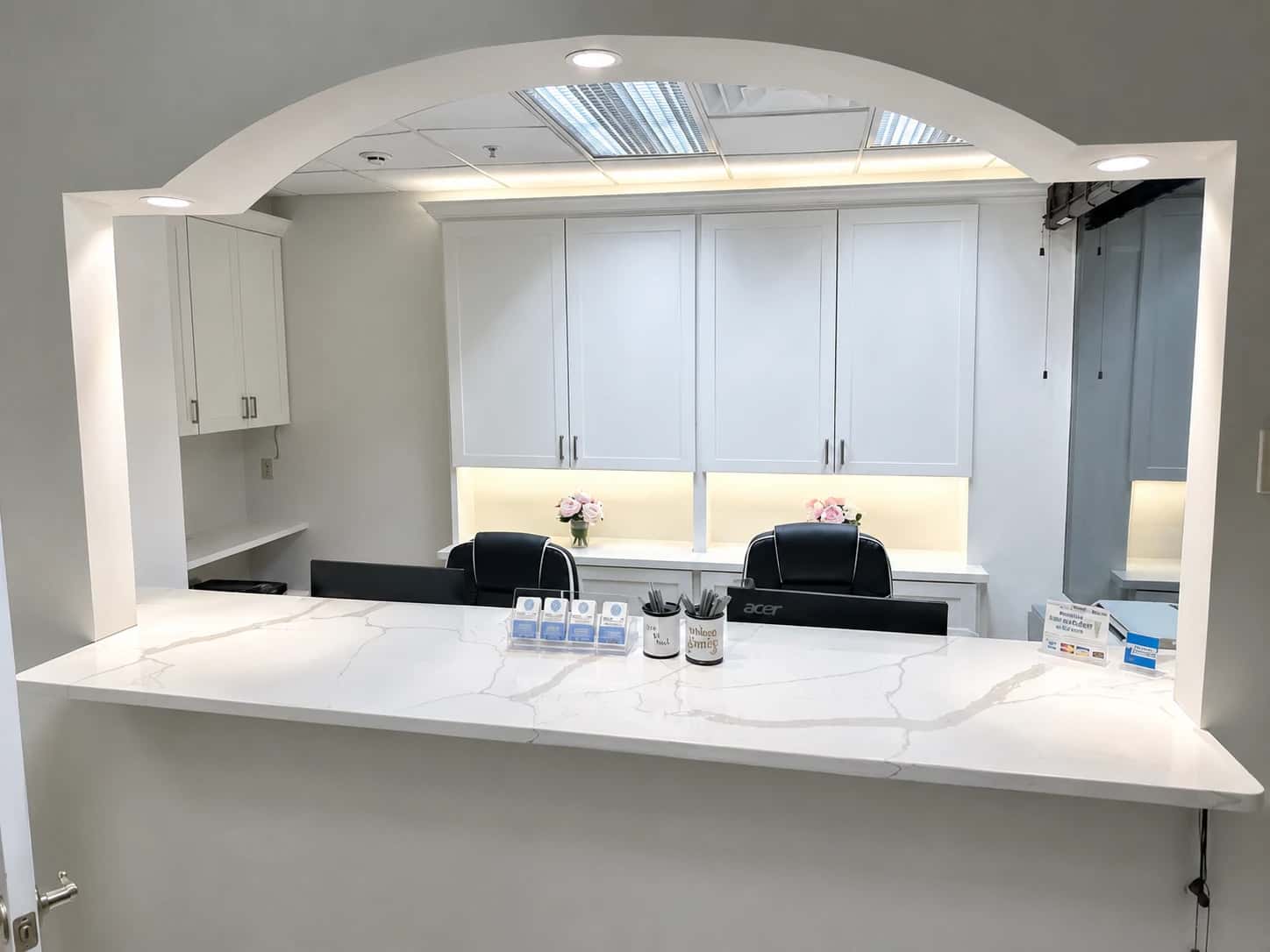 Completed medical and dental office reception by i30 Builders: an arched millwork opening over a Calacatta quartz front-desk counter with white shaker cabinetry and under-cabinet lighting.