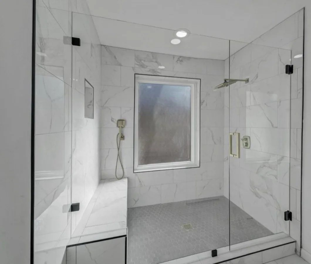 A frameless glass shower with marble-look tile, a built-in bench, a niche and a hex tile floor.
