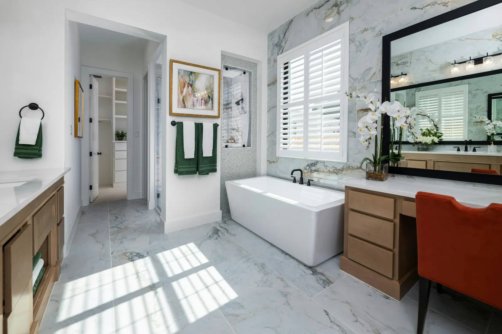 A marble primary bath with a freestanding tub, a vanity with a makeup station, and a walk-in shower beyond.