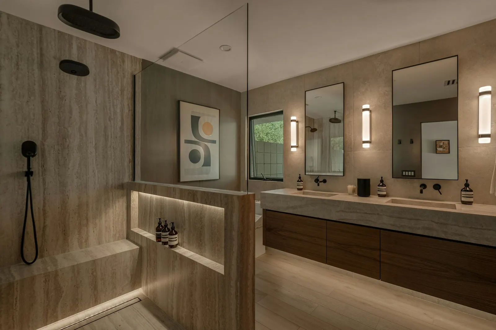 A primary bathroom with stone-clad walls, a walk-in shower with a lit niche and bench, and a floating walnut double vanity, built by i30 Builders.