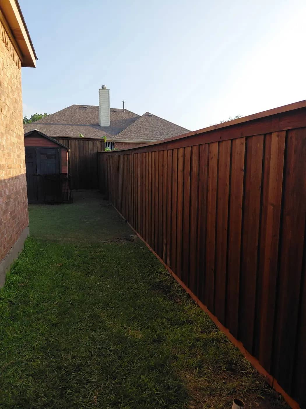 Capped board-on-board cedar fence running down a side yard, stained.