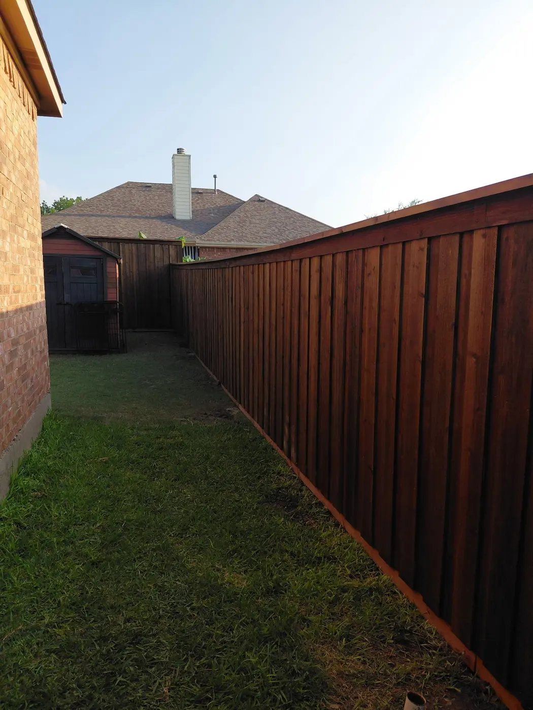Board-on-board cedar fence with a top cap down a side yard, stained dark walnut, Fate.