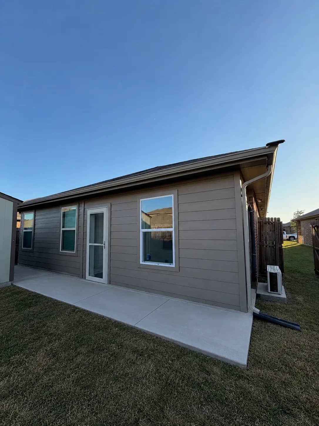The back of a house where a covered patio is now a closed-in room, with lap siding matched to the house, windows, a full-glass door and a mini-split condenser on a pad.