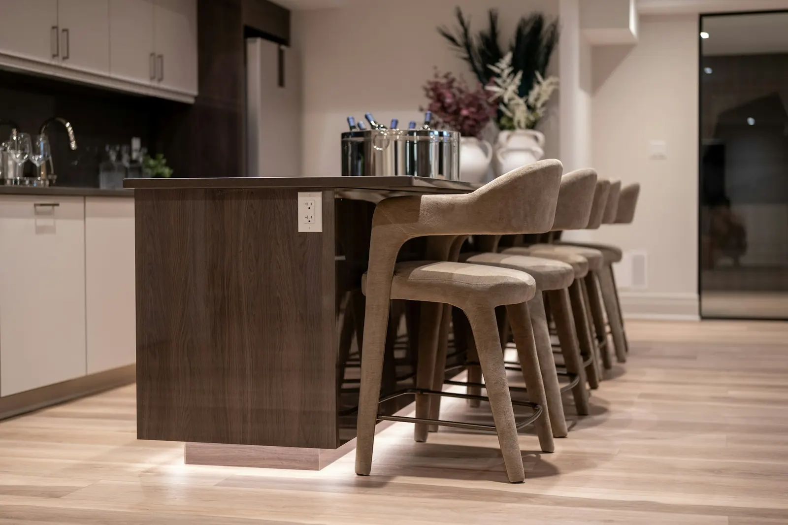 A walnut-finish kitchen island with upholstered seating and lighting under the base, built by i30 Builders.