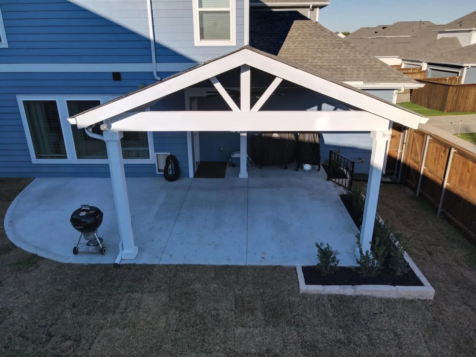 The same slab from the front: a new concrete patio with control joints and a curved edge, under a white gabled patio cover.