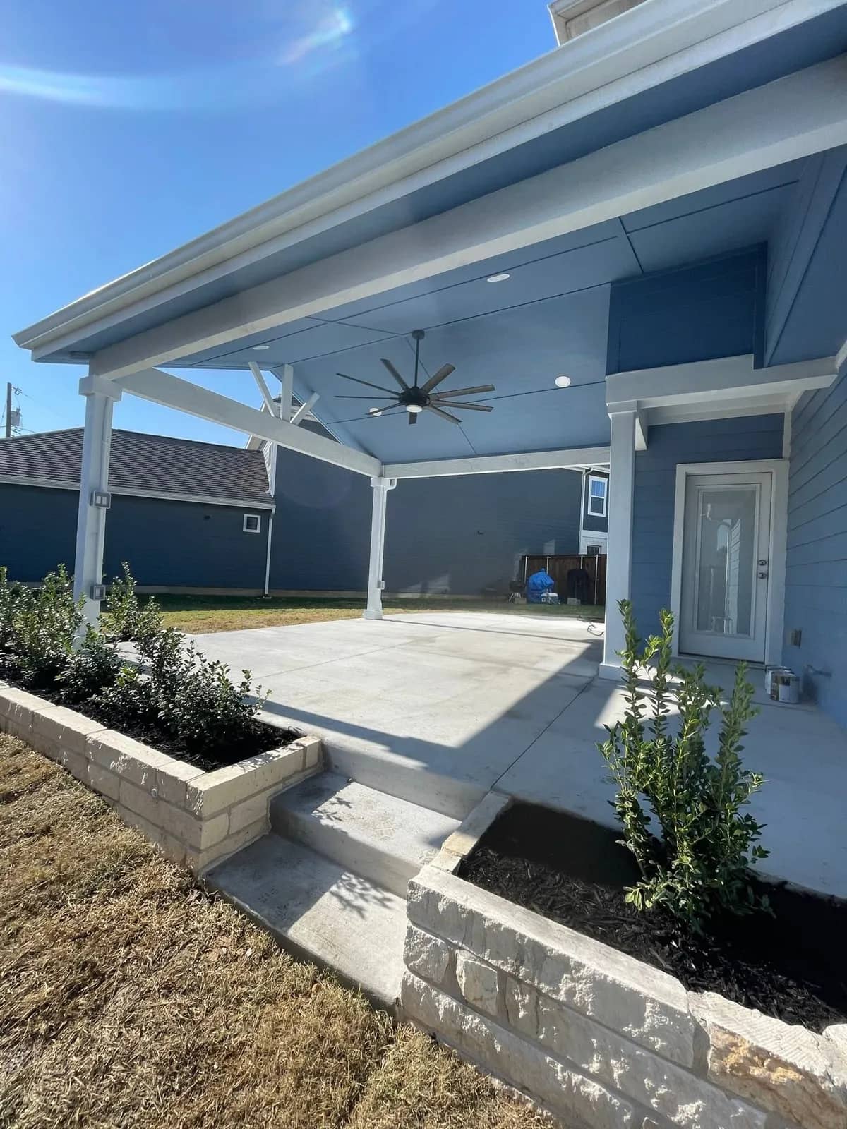 A low cut-limestone wall holding a raised planting bed beside new concrete steps up to a covered patio.