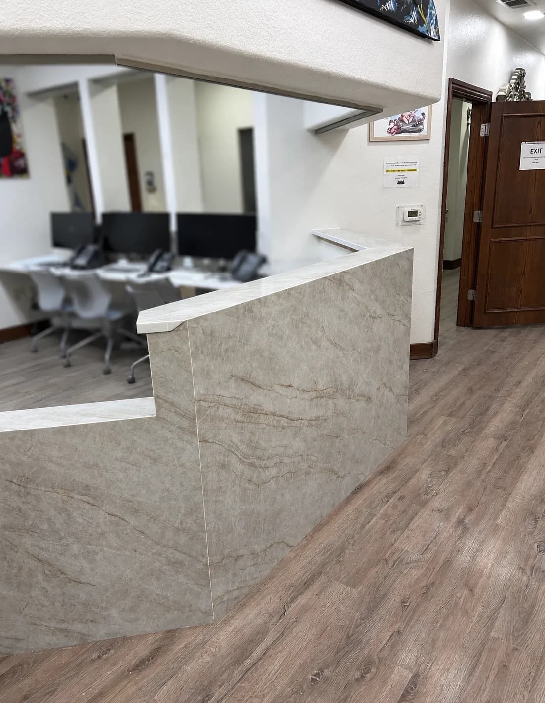 The same front desk rebuilt in full-height quartz waterfall panels with mitered corners and a raised transaction ledge, open to the staff work area.