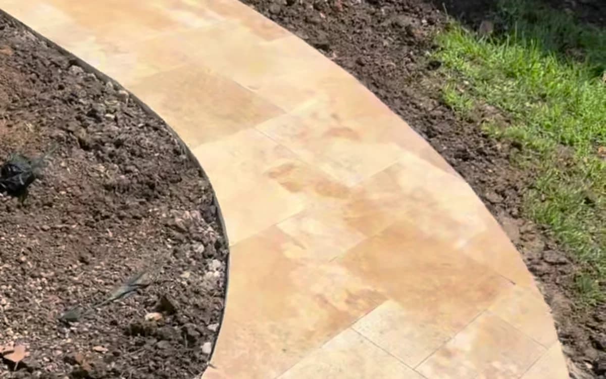 Curved travertine walkway with a concrete edge restraint along the bed.