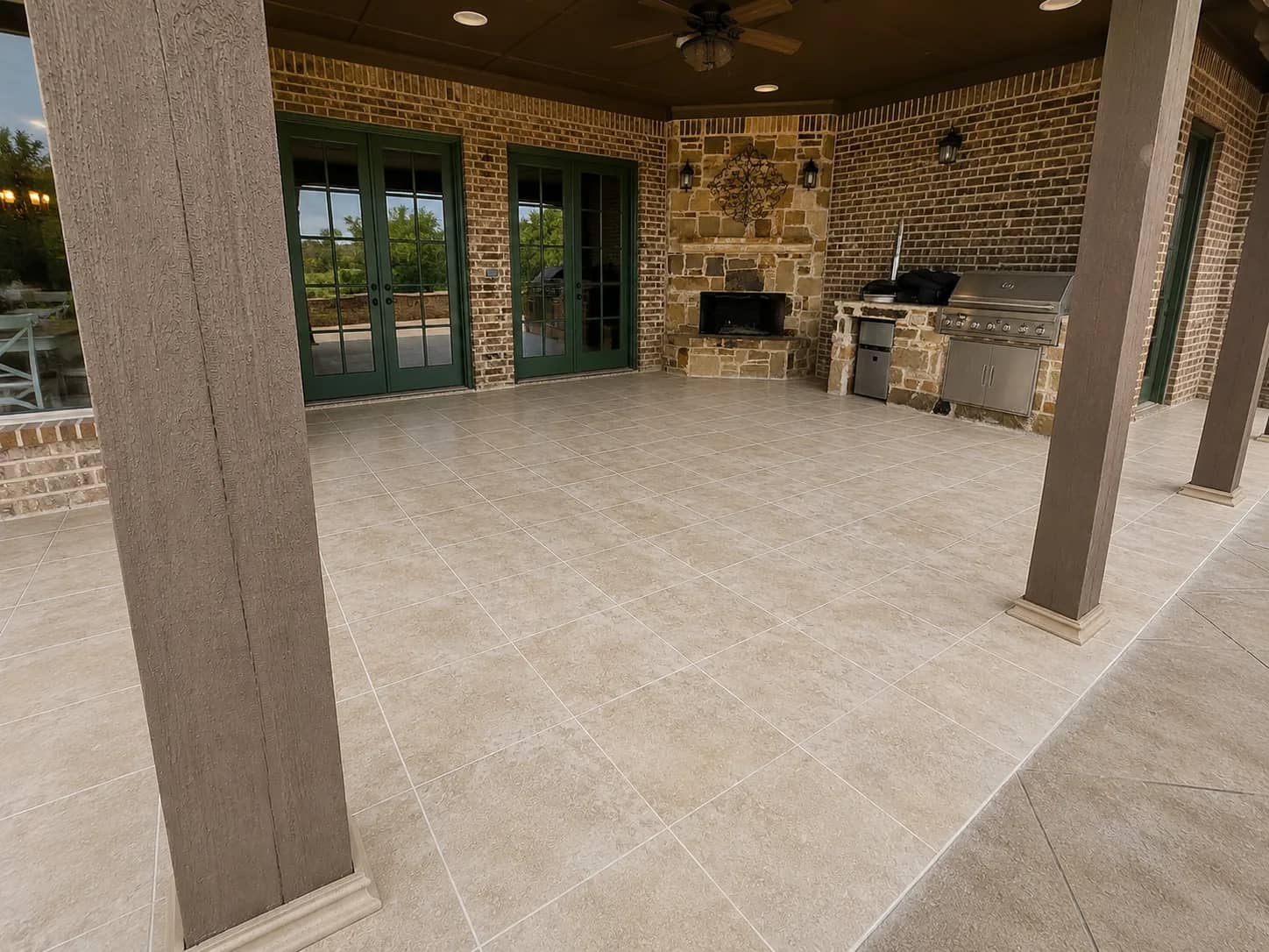 Covered patio with a stacked stone fireplace, a built-in stainless grill and a beverage refrigerator in a stone island, floored in ivory tile.