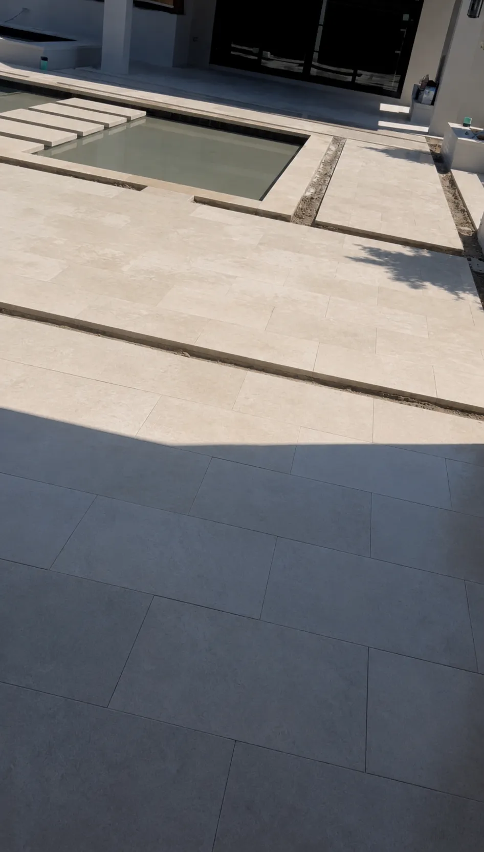 Pale stone pool deck with stepping pads across a water feature.